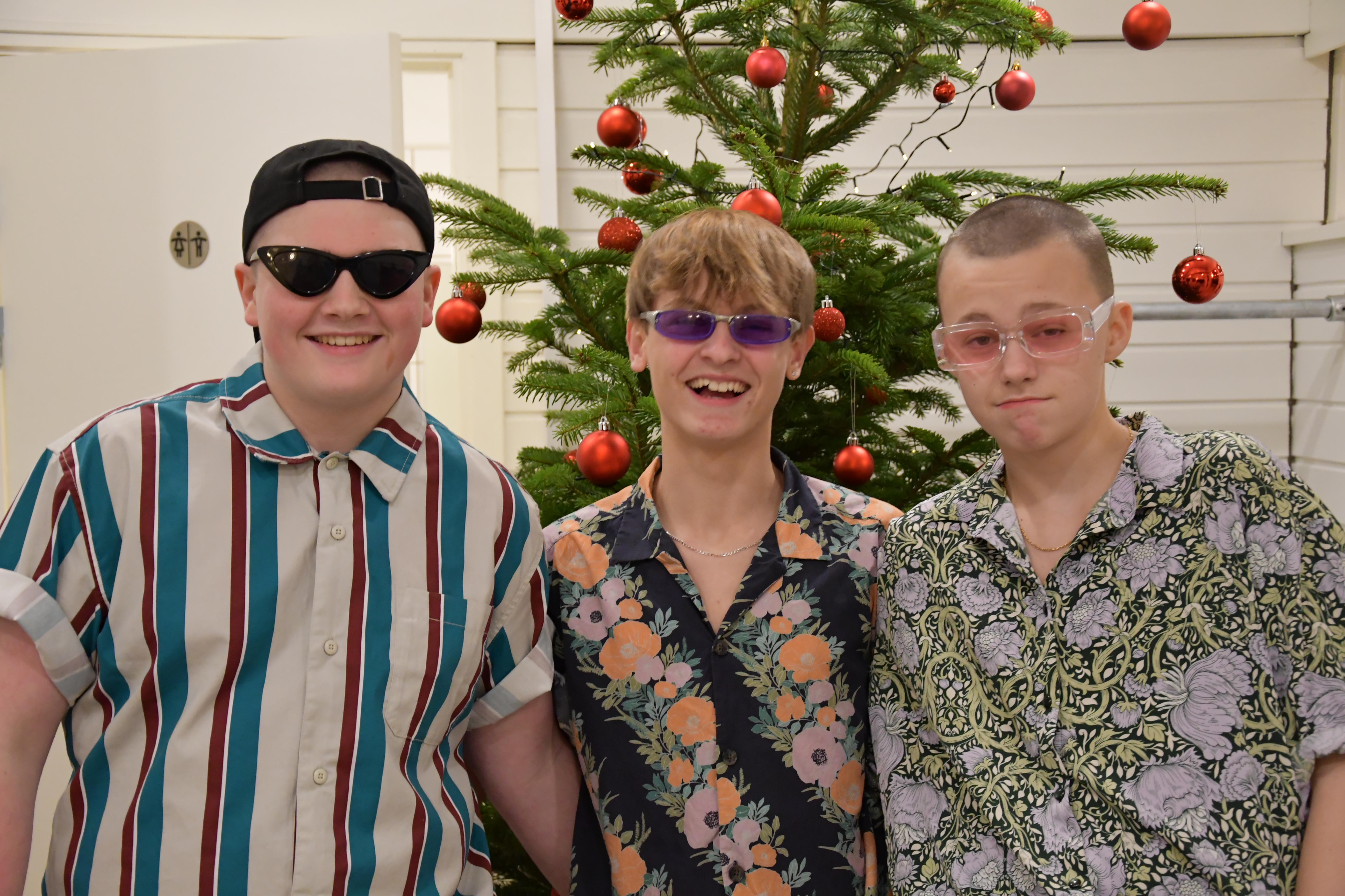 Tre drenge fra Sdr. Felding Efterskole som smiler og har mønstret skjorter på foran et juletræ